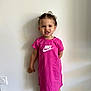 Kataleya a rejoint le concours — aidez-le/la à gagner de superbes lots ! toddler, child, girl, pink_dress, nike_logo, white_bow, standing, indoor, smile, teeth, hair, face, wall, floor, socks, wooden_floor, earrings, shadow, casual_clothing, portrait