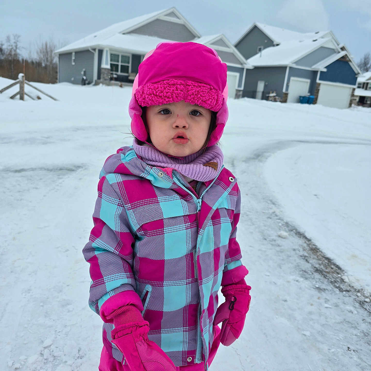 Lilya is registered to the contest to win money with this photo: child, cold_weather, curious, daytime, face, footwear, gloves, houses, jacket, neighborhood, outdoor, pants, person, pink_hat, playing_outside, scarf, snow, snowy_street, winter, winter_clothing