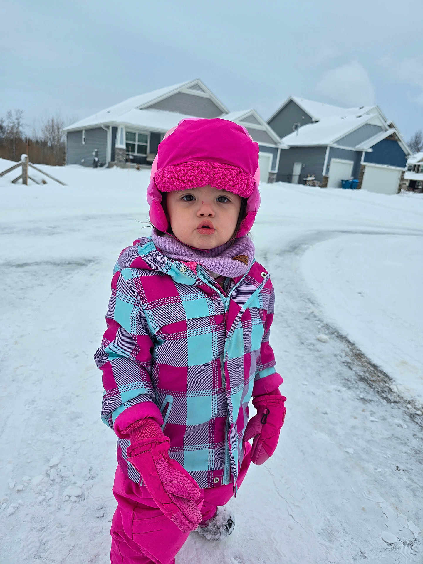 Lilya is registered to the contest to win money with this photo: child, cold_weather, curious, daytime, face, footwear, gloves, houses, jacket, neighborhood, outdoor, pants, person, pink_hat, playing_outside, scarf, snow, snowy_street, winter, winter_clothing