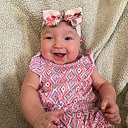 Kaylee is registered to the contest to win money with this photo: baby, smiling, headband, bow, romper, patterned_clothing, happy, infant, sitting, blanket, cozy, cute, child, face, hands, skin, indoors, portrait, closeup, wearing