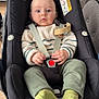 Milo participe au concours pour gagner de l'argent avec cette photo : baby, car_seat, maxi_cosi, child, infant, striped_sweater, green_pants, green_socks, indoor, living_room, couch, table, flowers, wooden_floor, person, face, seated, safety_harness, neutral_expression, home