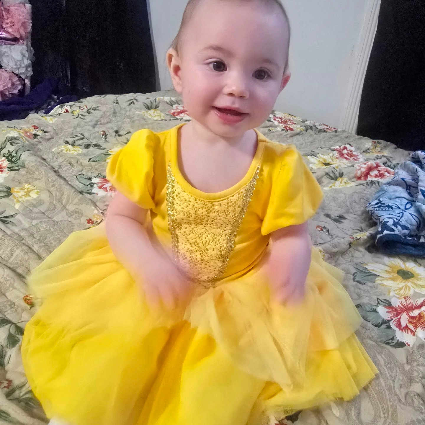 Gracelynne joined the competition — help win amazing prizes! baby, bed, child, clothing, cute, face, floral_bedspread, hands, happy, indoor, person, portrait, room, sitting, smiling, soft_lighting, toddler, white_tights, yellow_dress, young_child