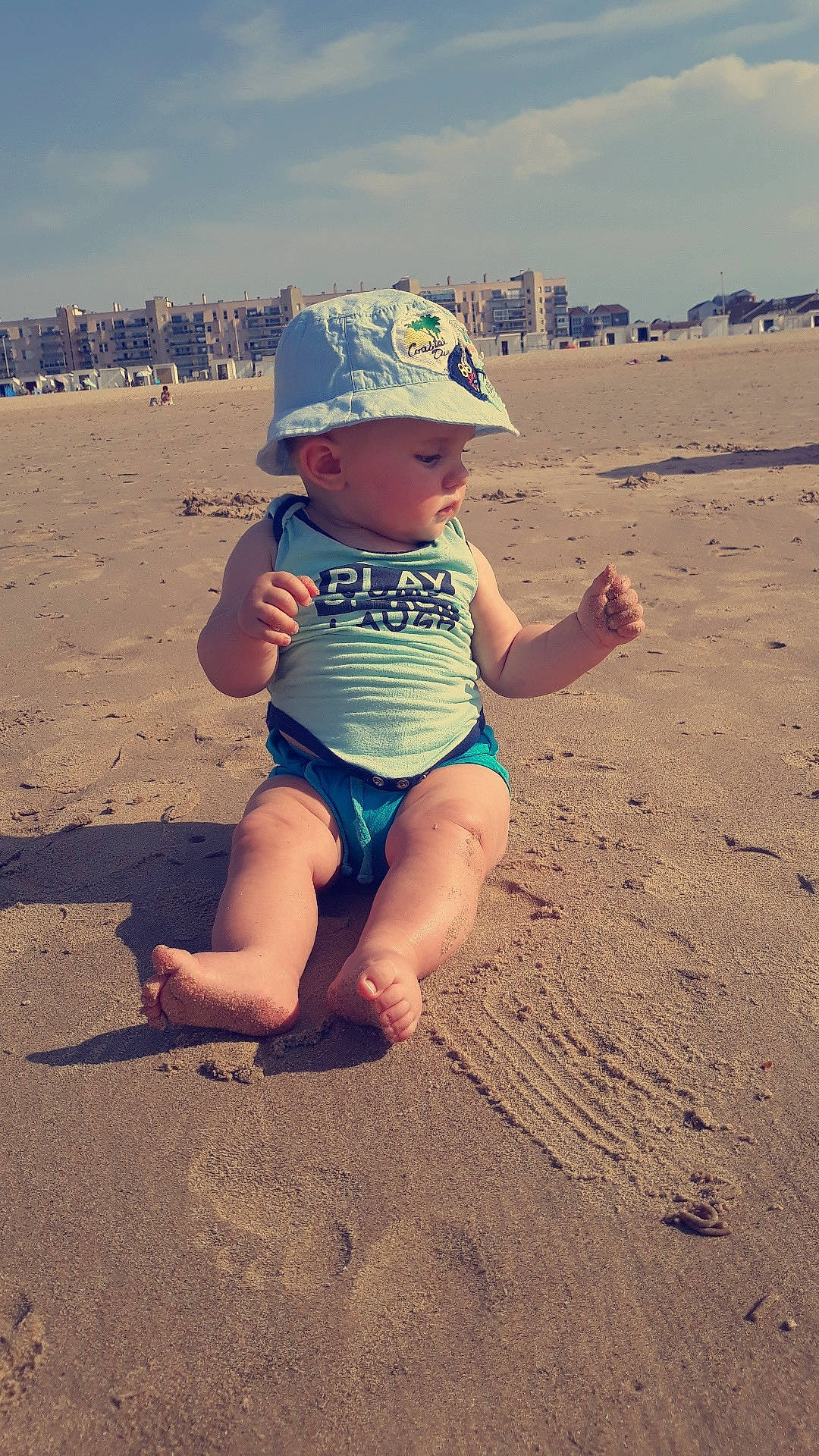 Léo a rejoint le concours — aidez-le/la à gagner de superbes lots ! barefoot, beach, child, fawn, fun, hat, headgear, headwear, landscape, leg, person, play, sand, singing_sand, sitting, smile, summer, sun_hat, toddler, vacation
