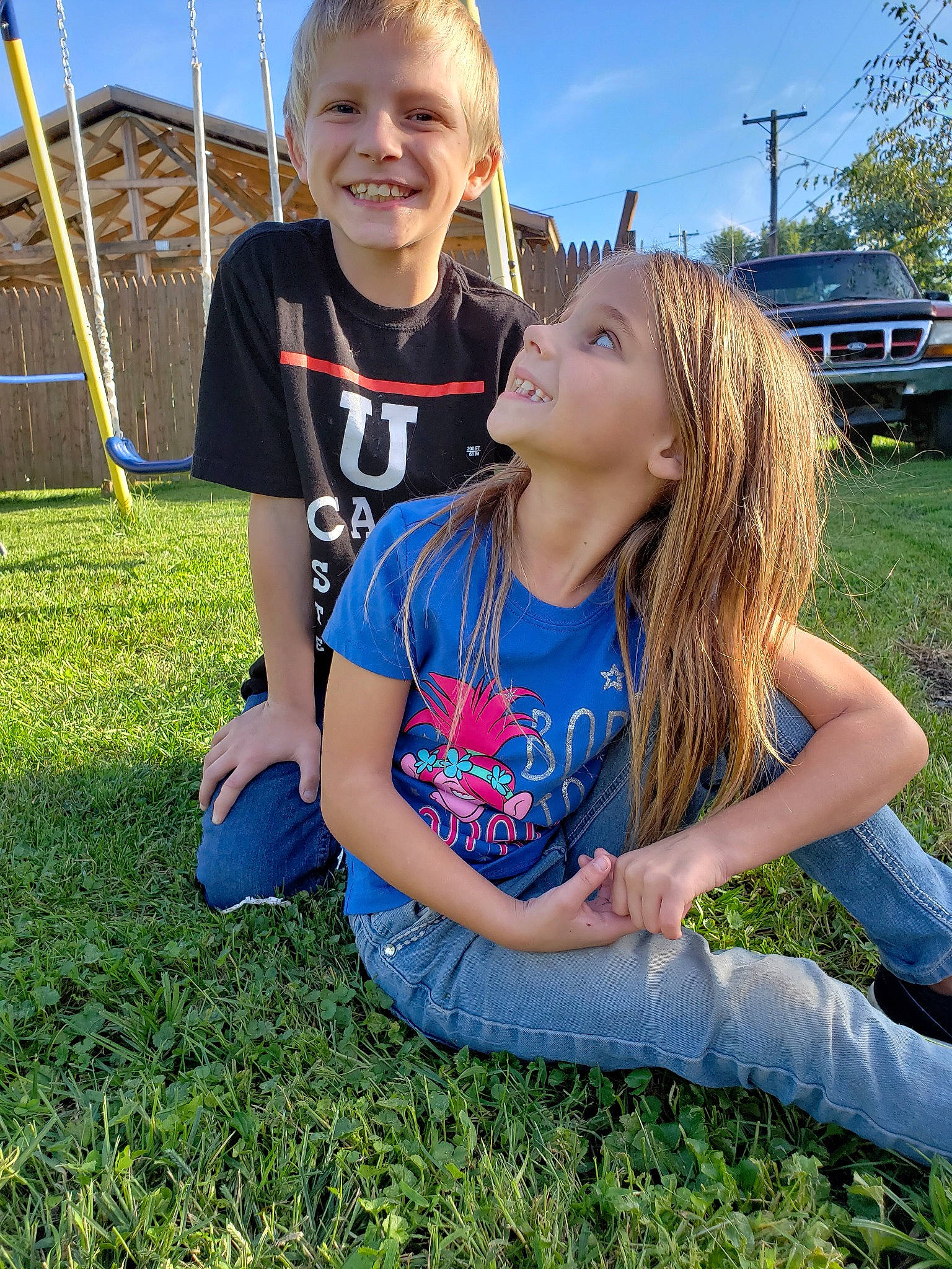 Johnathan is registered to the contest to win money with this photo: blond, child, facial_expression, friendship, fun, grass, grass_family, happy, joy, lawn, long_hair, person, photography, plant, playground, sibling, sitting, smile, summer, t_shirt