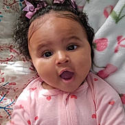 Estella is registered to the contest to win money with this photo: baby, infant, child, portrait, lying_down, wide_eyes, open_mouth, curly_hair, hair_bows, pink_onesie, hearts, floral_bedding, blanket, bedding, cozy, indoor, close_up, smiling, adorable, photography