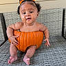 Estella joined the competition — help win amazing prizes! baby, child, infant, pumpkin_costume, halloween, orange, hair_bows, curly_hair, sitting, chair, wicker_furniture, portrait, indoors, outdoors, smiling, adorable, barefoot, costume, photography, playful