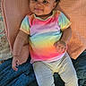 Estella joined the competition — help win amazing prizes! baby, child, infant, smiling, portrait, indoors, bed, blanket, quilt, pink_bows, curly_hair, rainbow_shirt, gray_pants, sneakers, fashion, lying_down, happy, face, colorful, home