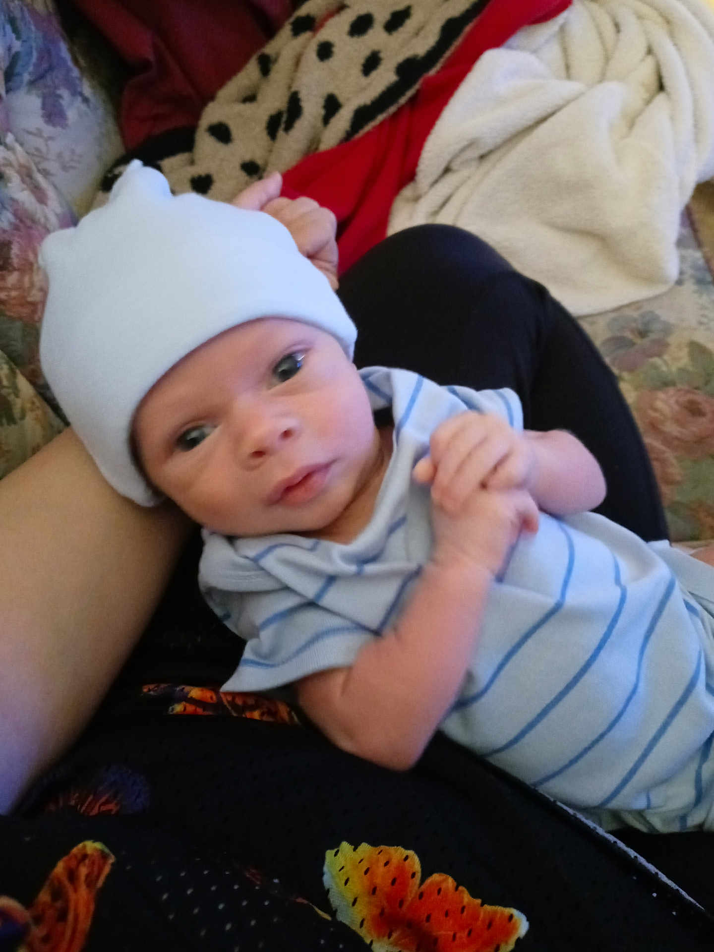 Andrew is registered to the contest to win money with this photo: baby, infant, hat, blue_clothing, striped, hands, face, eyes, couch, blanket, fabric, person, indoor, closeup, newborn, skin, arm, resting, holding, soft
