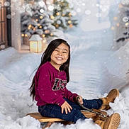 Armani is registered to the contest to win money with this photo: child, smiling, sled, snow, winter, boots, long_hair, outdoor, holiday, joy, tree, lantern, blurred_background, cold_weather, casual_clothing, sitting, fun, playful, snowy_scene, happy