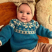 Alix a rejoint le concours — aidez-le/la à gagner de superbes lots ! baby, child, smiling, knitted_hat, blue_sweater, beige_pants, blanket, teddy_bear, soft_texture, cute, portrait, indoors, cozy, happy, infant, person, warm_colors, headwear, comfortable, lying_down