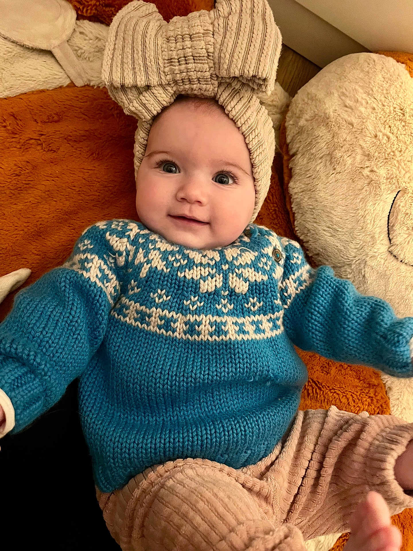 Alix a rejoint le concours — aidez-le/la à gagner de superbes lots ! baby, child, smiling, knitted_hat, blue_sweater, beige_pants, blanket, teddy_bear, soft_texture, cute, portrait, indoors, cozy, happy, infant, person, warm_colors, headwear, comfortable, lying_down