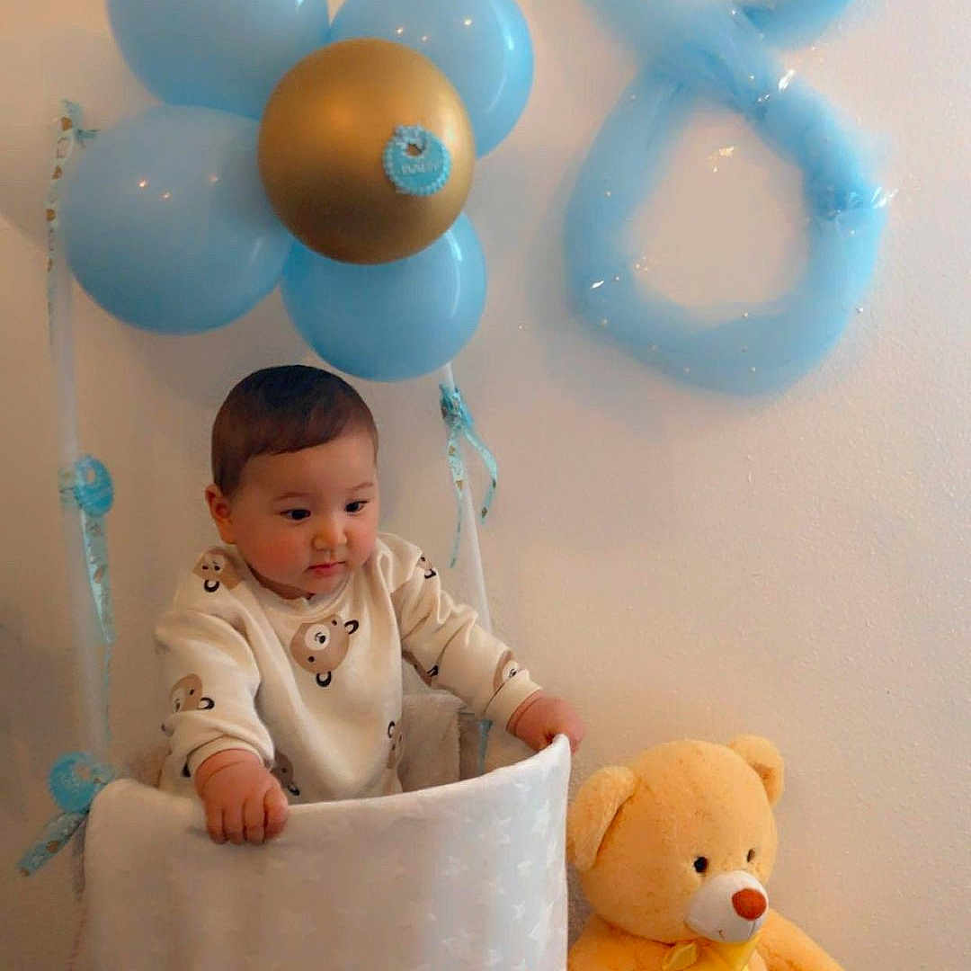 Liam participe au concours pour gagner de l'argent avec cette photo : baby, balloon, basket, birthday, blue_balloon, carpet, celebration, child, childrens_clothing, cute, decor, gold_balloon, indoors, number_balloon, person, smiling, stuffed_animal, teddy_bear, toy, wall