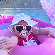 Isla Jean joined the competition — help win amazing prizes! baby, child, infant, pool, inflatable_pool, pink, sunglasses, heart_shaped_sunglasses, sun_hat, pacifier, outdoor, summer, swimwear, seated, portrait, playful, vacation, adult_hand, colorful, photograph