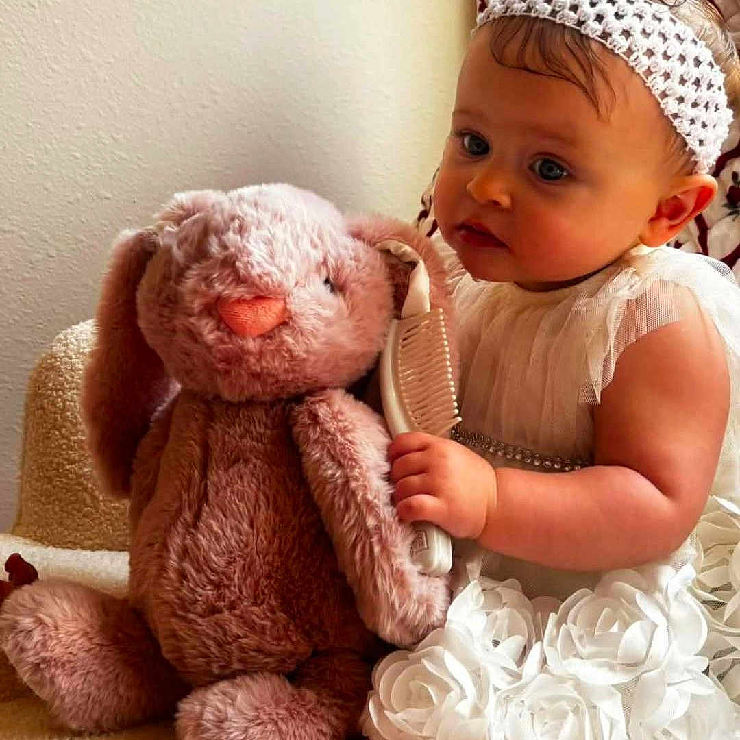 Isla Jean joined the competition — help win amazing prizes! baby, child, toddler, portrait, sitting, indoors, smiling, serious_expression, headband, white_dress, frilly_dress, teddy_bear, stuffed_animal, toy, comb, grooming, chair, cozy, warm_lighting, candid