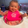 Isla Jean is registered to the contest to win money with this photo: baby, child, infant, smiling, happy, portrait, high_chair, bib, pink_clothing, dress, indoor, home, nursery, playpen, sippy_cup, table, seated, curly_hair, looking_at_camera, family_photo