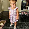 child, girl, pigtails, dress, silver_shoes, smile, floor, tile_floor, indoor, home, chair, patterned_chair, door, black_floor, happy, person, young_child, short_sleeves, playful, cute