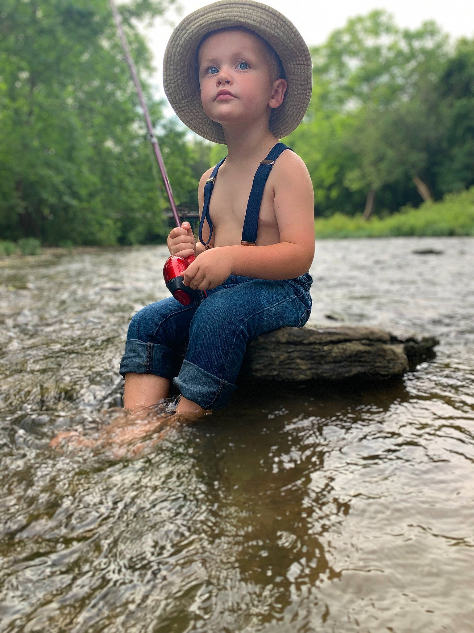 Merrick is registered to the contest to win money with this photo: bank, face, fun, grass, happy, hat, head, lake, leisure, nature, outdoor_recreation, people_in_nature, person, recreation, shorts, summer, sun_hat, toddler, tree, water