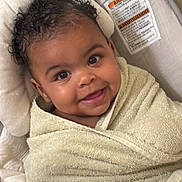 Elora joined the competition — help win amazing prizes! baby, child, smiling, towel, curly_hair, face, infant, cushion, seat, warning_label, indoors, cozy, wrapped, portrait, cute, happy, young_child, skin, head, expression