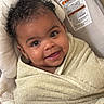 baby, child, smiling, towel, curly_hair, face, infant, cushion, seat, warning_label, indoors, cozy, wrapped, portrait, cute, happy, young_child, skin, head, expression
