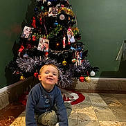 Dylan participe au concours pour gagner de l'argent avec cette photo : casual_clothing, child, christmas_tree, cozy, decorations, family_photos, festive, floor, green_wall, happy, holiday, holiday_decor, indoor, ornaments, red_balls, sitting, smiling, tiled_floor, tinsel, young_child