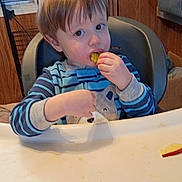 áxel joined the competition — help win amazing prizes! toddler, child, high_chair, striped_pajamas, pickle, eating, indoor, wood_paneling, window, star_decorations, messy_tray, face, person, furniture, clothing, hand, food, snack, young_child, baby