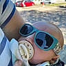 baby, sunglasses, pacifier, arm, striped_shirt, outdoor, daylight, car, building, hand, clothing, face, person, headwear, reflection, child, holding, cute, sunlight, casual