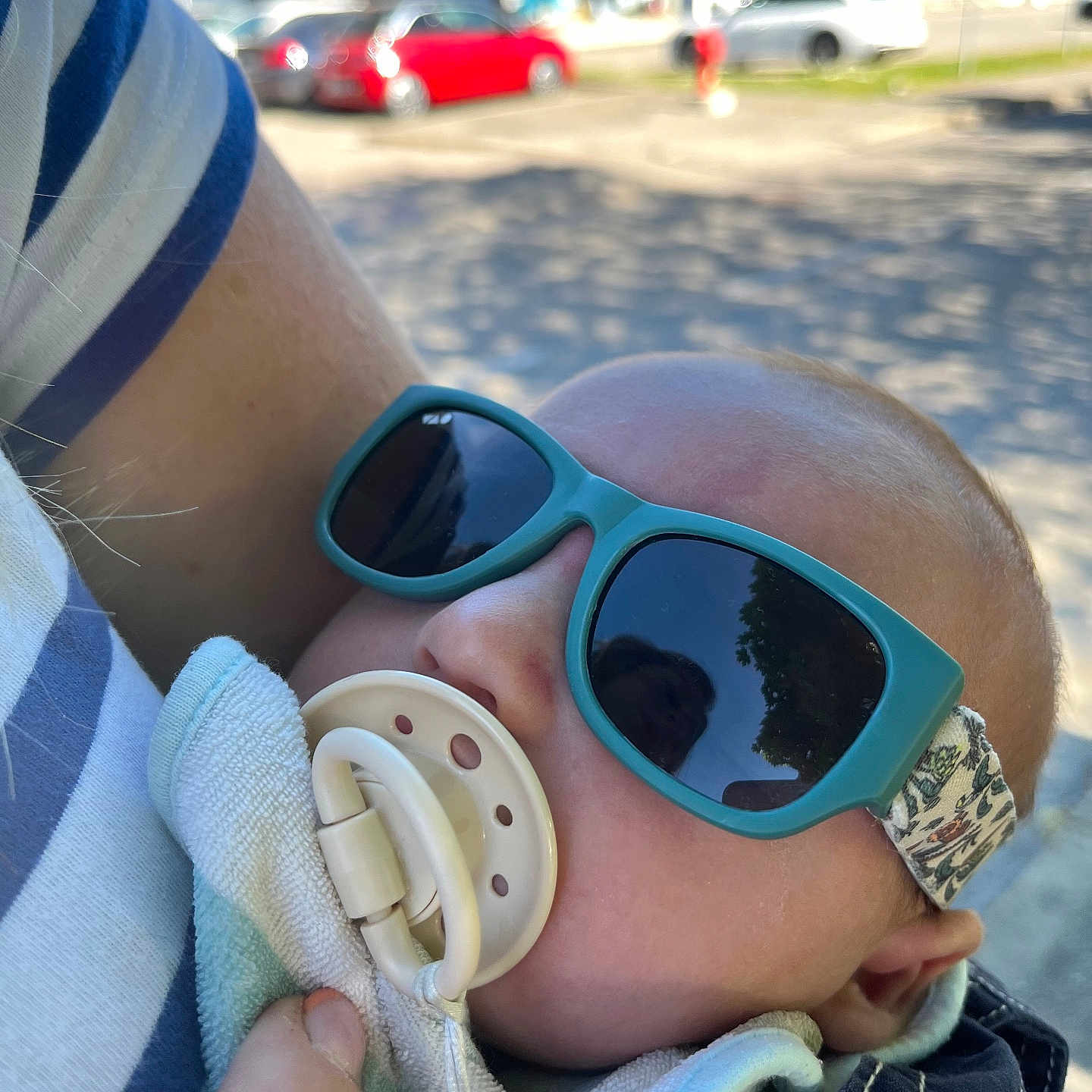 Jules a rejoint le concours — aidez-le/la à gagner de superbes lots ! baby, sunglasses, pacifier, arm, striped_shirt, outdoor, daylight, car, building, hand, clothing, face, person, headwear, reflection, child, holding, cute, sunlight, casual