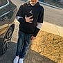child, boy, standing, hoodie, jeans, sneakers, car, street, suburb, daylight, spiked_hair, sidewalk, residential, driveway, road, sunlight, outdoor, person, casual_wear, parking