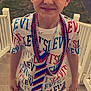child, boy, face_paint, beaded_necklaces, tshirt, shorts, crocs, stairs, outdoor, sidewalk, grass, red_truck, yellow_trash_bin, white_fence, smiling, blond_hair, casual_clothing, summer, portrait, happy