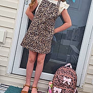 Heaven is registered to the contest to win money with this photo: child, girl, glasses, headband, leopard_print, dress, backpack, pink_bows, doormat, door, flower_wreath, smile, sandals, concrete, house_exterior, window, reflection, outdoor, standing, accessory