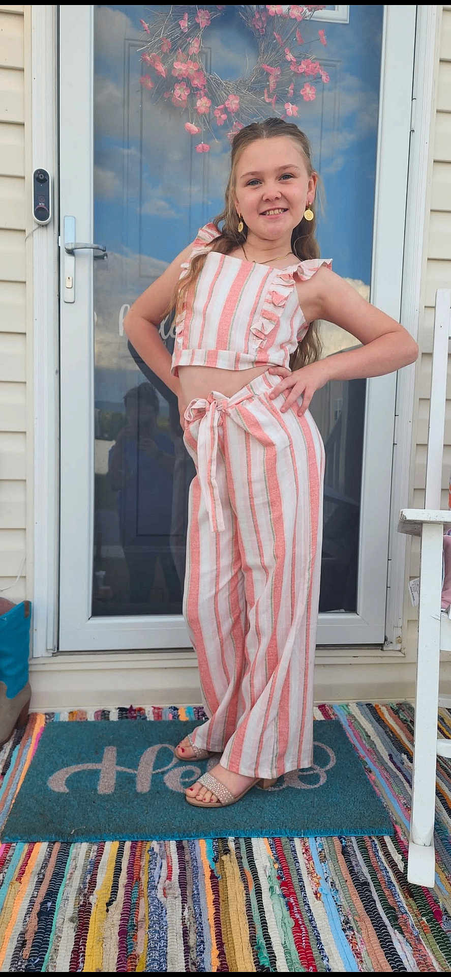 Heaven is registered to the contest to win money with this photo: child, girl, smile, pose, striped_clothing, pants, top, sandals, earrings, wreath, door, glass_door, doormat, rug, outdoor, home_entrance, hand_on_hip, long_hair, fashion, accessories