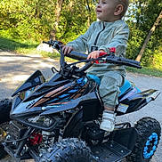 Hayden a rejoint le concours — aidez-le/la à gagner de superbes lots ! child, toddler, atv, toy_vehicle, outdoor, trees, greenery, sunlight, road, happy, smiling, clothing, shoes, nature, vehicle, wheels, play, daytime, person, recreation