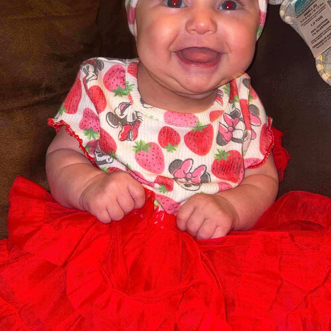 Audrey is registered to the contest to win money with this photo: accessories, baby, bonnet, clothing, costume, couch, cushion, dress, face, furniture, happy, hat, head, homedecor, laughing, person, photography, portrait, sitting, skirt