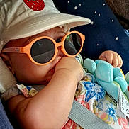 Caitlin a rejoint le concours — aidez-le/la à gagner de superbes lots ! baby, child, sunglasses, hat, strawberry_patch, thumb_sucking, car_seat, seatbelt, plush_toy, floral_clothing, infant, cute, orange_glasses, blue_toy, pacifier, relaxed, indoor, portrait, casual, comfortable