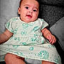 baby, infant, child, cute, smiling, drooling, dress, cartoon_print, sitting, couch, pillow, cozy, indoors, skin, foot, hand, face, happy, relaxed, portrait