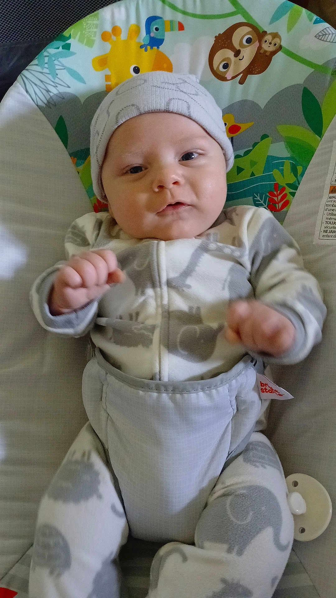 Koen is registered to the contest to win money with this photo: baby, infant, child, onesie, hat, baby_seat, animal_print, elephant, giraffe, toucan, sloth, pacifier, cute, face, indoor, comfort, clothing, young_child, person, smiling