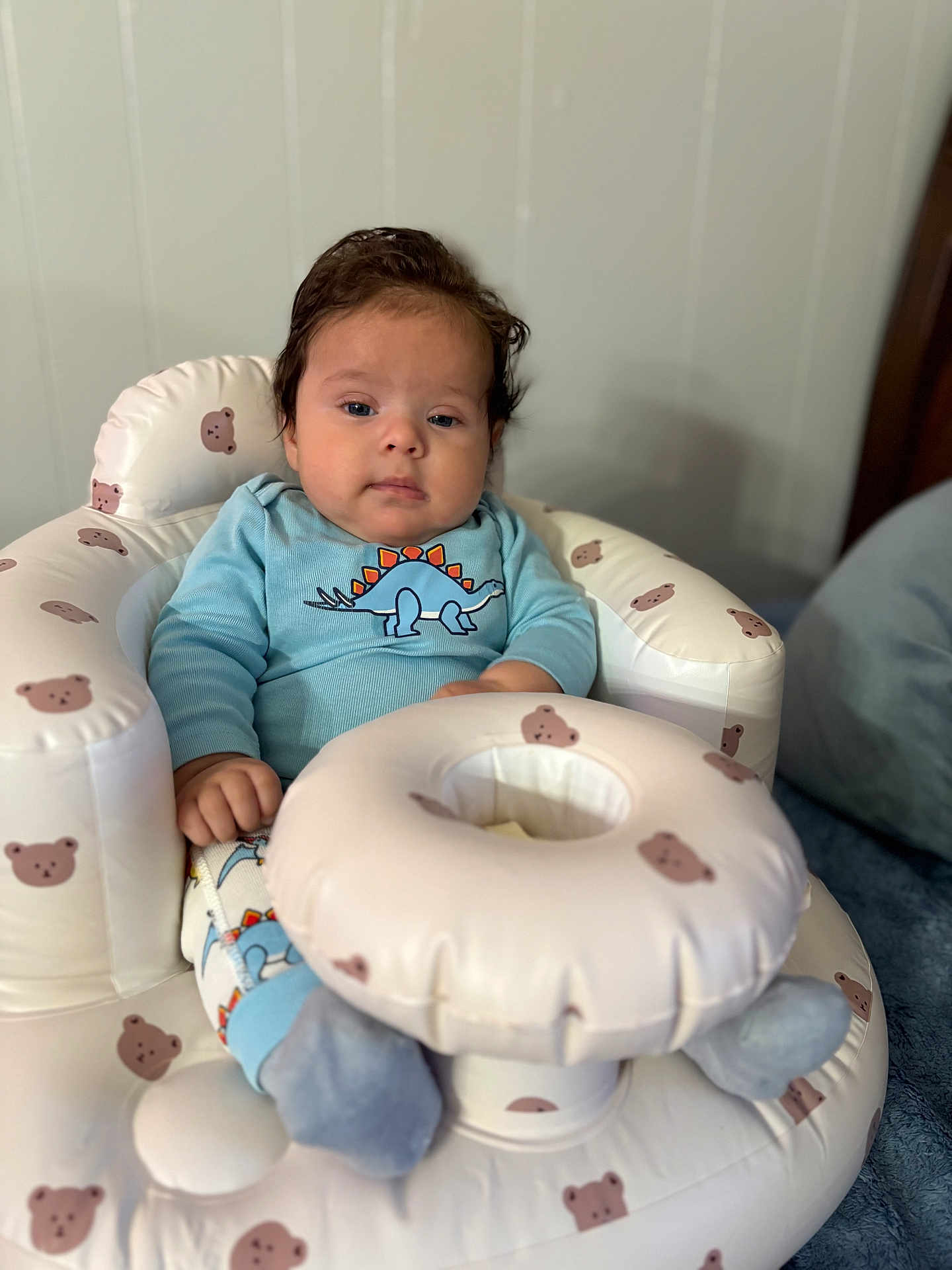 Gael is registered to the contest to win money with this photo: baby, child, infant, dinosaur_clothing, blue_clothing, inflatable_chair, bear_pattern, socks, indoor, soft_toys, cute, face, person, seated, plush, young_child, comfort, relaxed, portrait, home