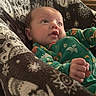 animal_pattern, baby, blanket, child, close_up, couch, cozy, curious, eyes, face, family_photo, fist, green_outfit, hand, indoors, infant, lying_down, pajamas, portrait, soft_lighting