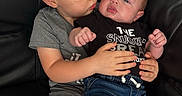 Bentley is registered to the contest to win money with this photo: baby, toddler, siblings, brother, infant, child, kiss, cuddling, sitting, couch, indoor, portrait, family, smiling, adorable, denim, onesie, bare_feet, black_couch, home