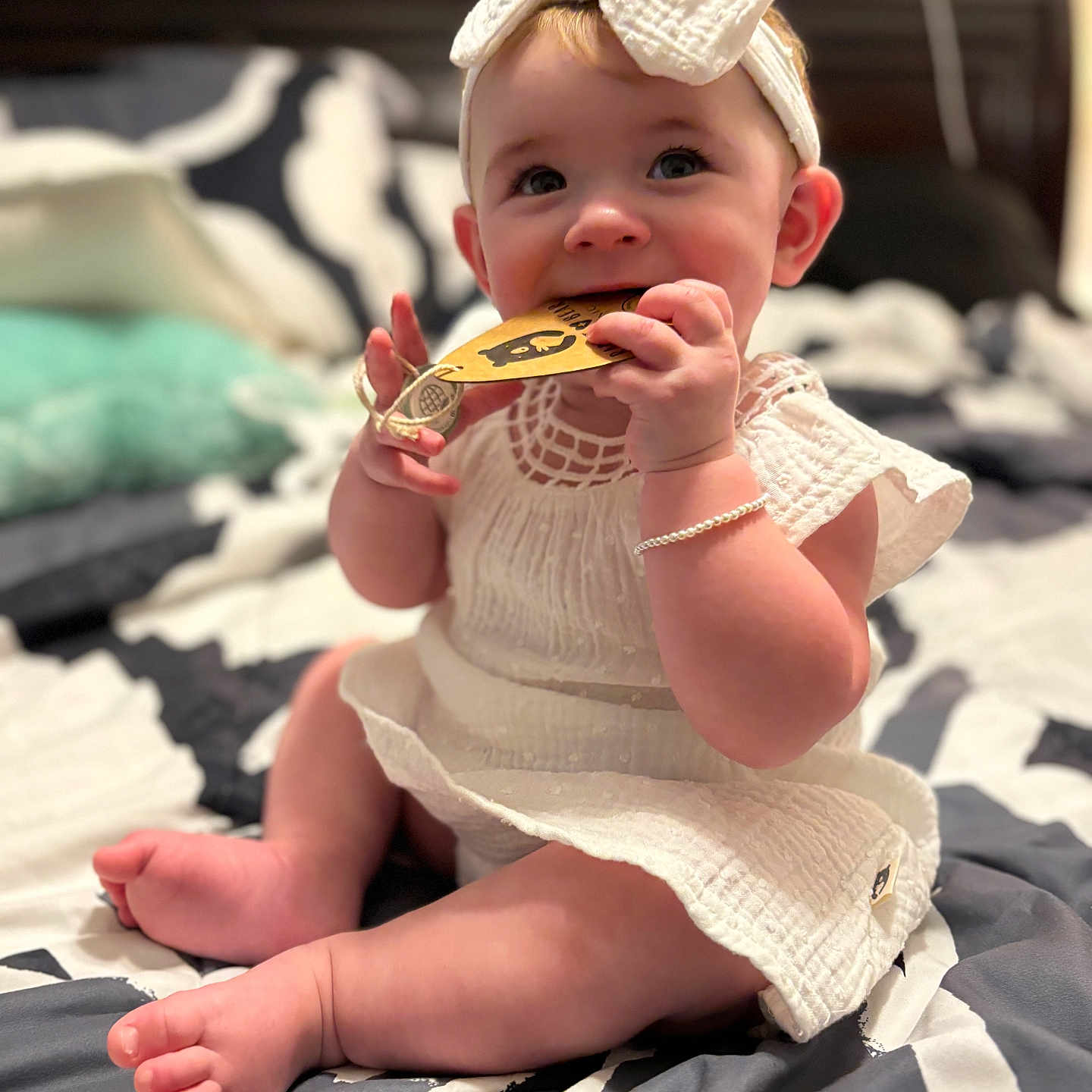 Lydia is registered to the contest to win money with this photo: baby, bed, bedding, bow, bracelet, chewing, child, cute, foot, hand, headband, indoors, infant, pillow, sitting, skin, smiling, soft_light, tag, white_dress