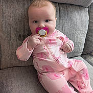 River is registered to the contest to win money with this photo: baby, infant, child, sitting, couch, cushion, pacifier, pink_outfit, elephant_pattern, onesie, portrait, indoor, cozy, gray_background, short_hair, looking_at_camera, calm, cute, soft_lighting, home