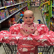 Eowyn joined the competition — help win amazing prizes! baby, shopping_cart, toy_store, toys, aisle, pink, elephant_pattern, child, smiling, clothing, floor, shopping, retail, cute, infant, socks, person, store_shelves, happy, indoor