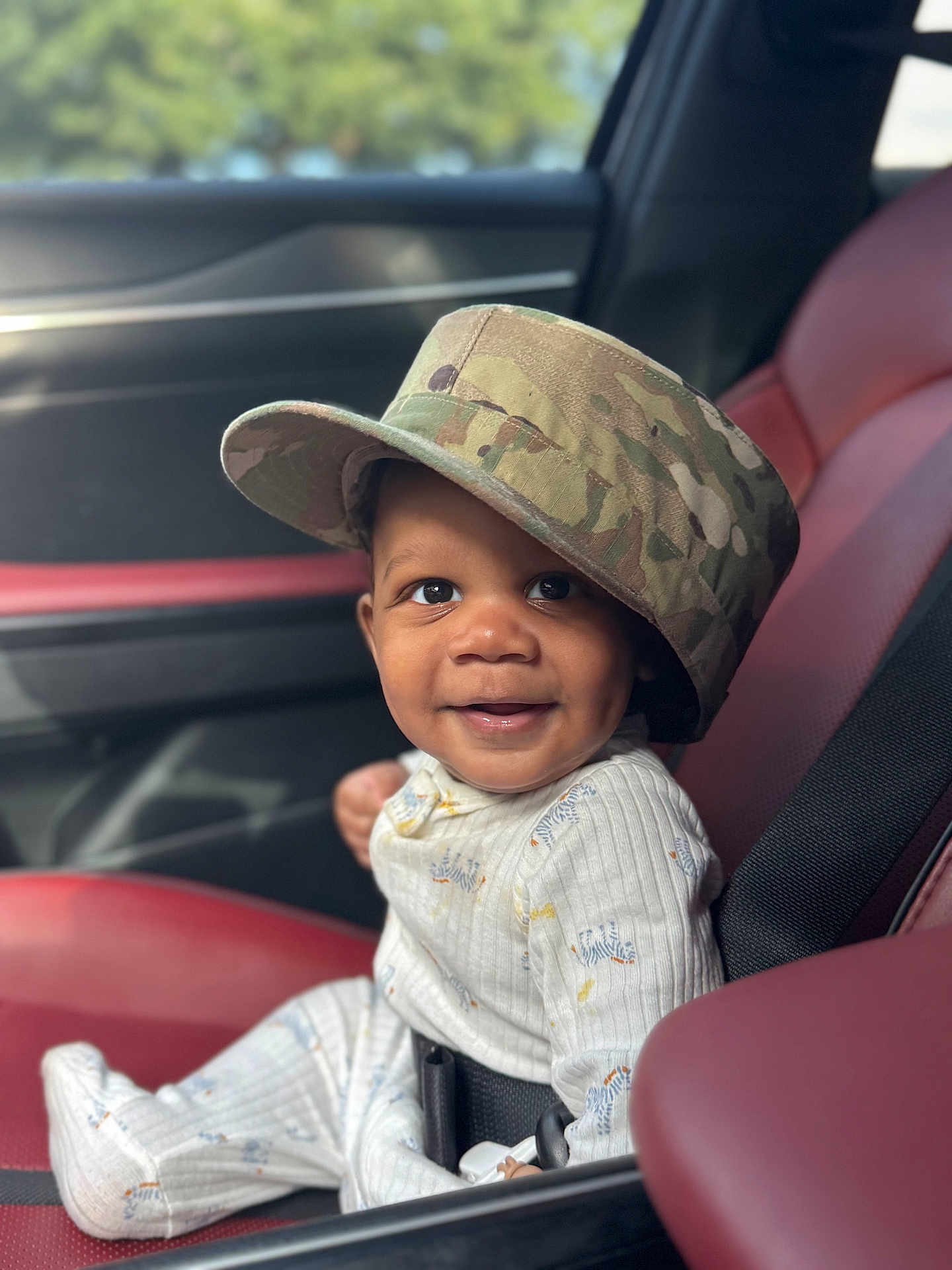Jasiah joined the competition — help win amazing prizes! baby, child, smile, car_seat, hat, camouflage, clothing, infant, face, portrait, seatbelt, car_interior, red_seat, black_seatbelt, cute, happy, young_child, sitting, indoors, person