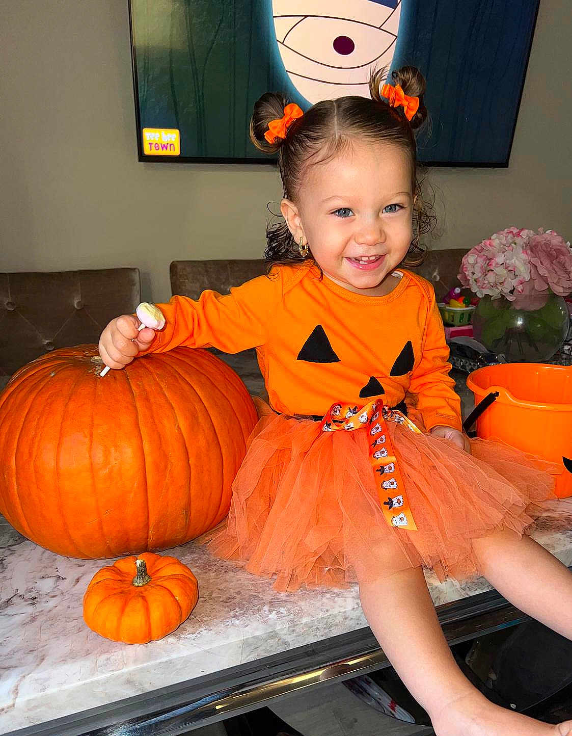 Monroe Blu is registered to the contest to win money with this photo: child, toddler, pumpkin, orange, dress, tutu, smile, table, lollipop, hair_bows, indoor, flower_vase, flowers, bucket, marble_table, happy, cute, holiday, festive, decoration