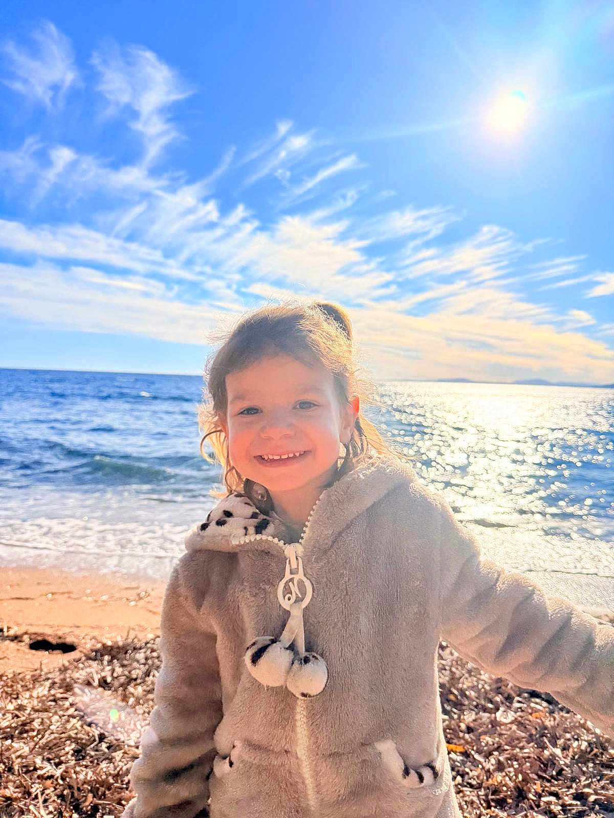 Céleste a rejoint le concours — aidez-le/la à gagner de superbes lots ! child, smiling, beach, ocean, sunlight, sky, clouds, water, jacket, cozy, happy, outdoor, nature, seashore, sand, waves, portrait, sun, holiday, warm_clothing