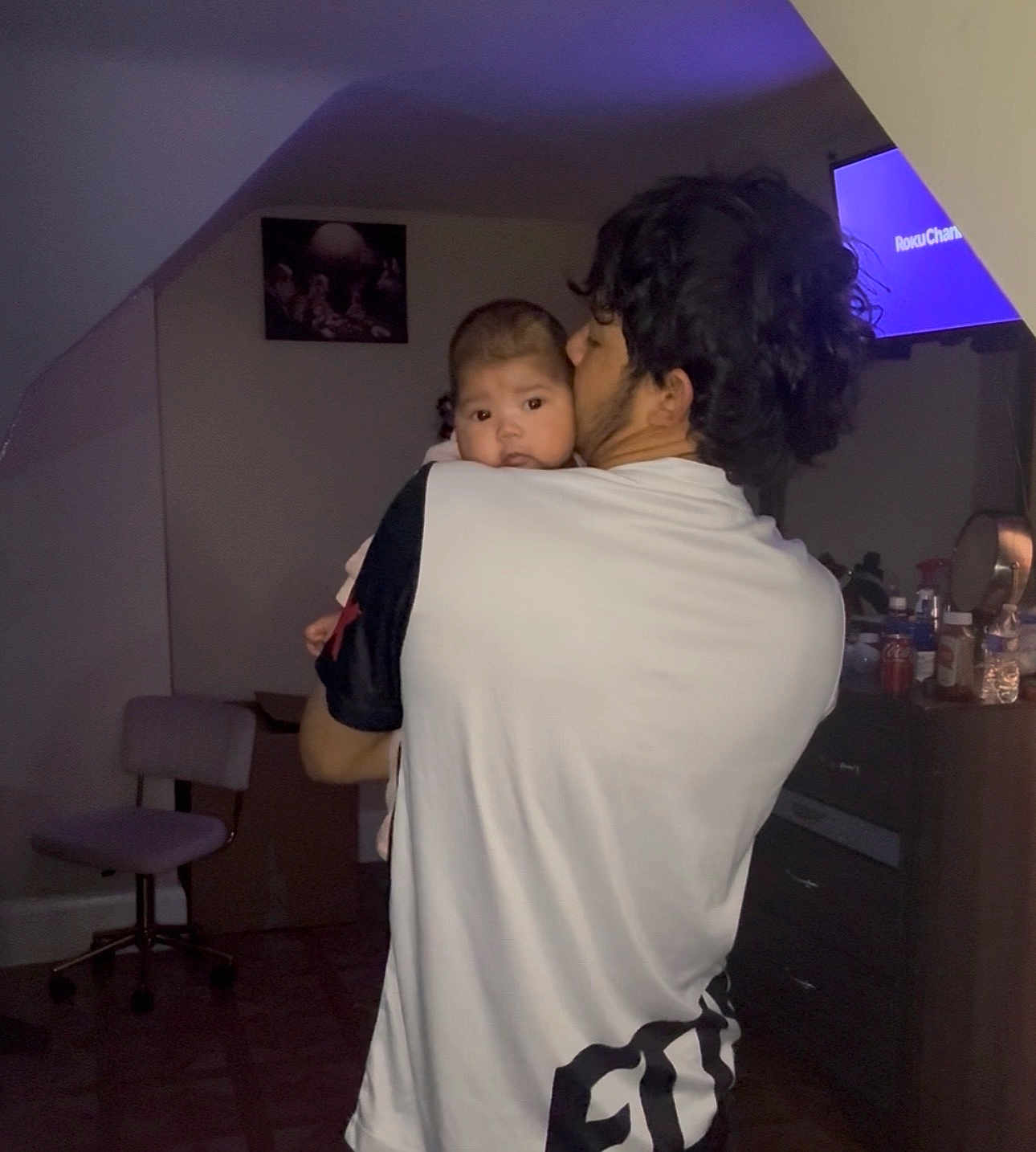 Arly is registered to the contest to win money with this photo: baby, man, indoor, holding, kiss, television, furniture, chair, dresser, curious, dim_light, person, room, head, face, clothing, home, floor, cabinet, portrait