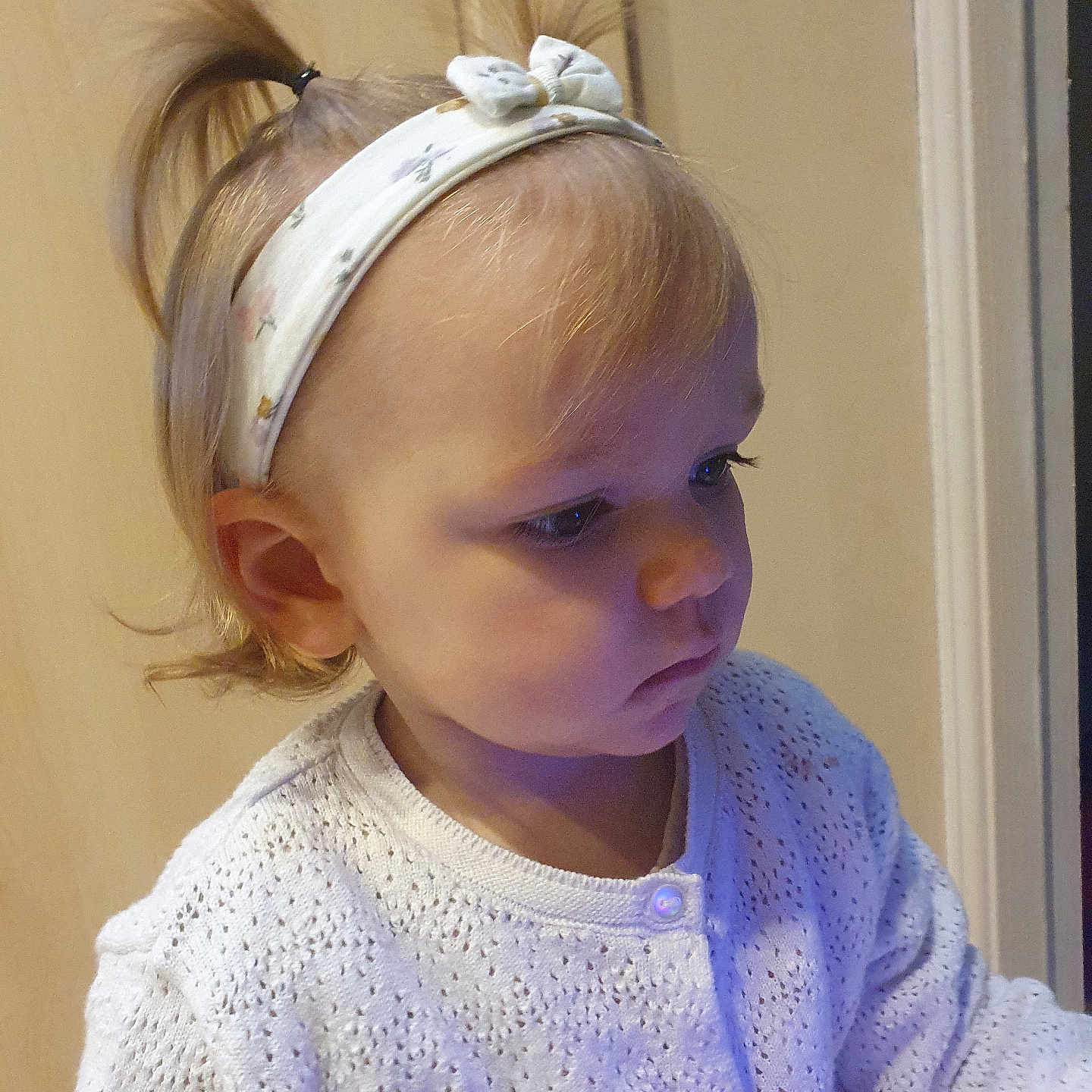 Mya participe au concours pour gagner de l'argent avec cette photo : toddler, child, person, headband, ponytail, white_sweater, knitwear, portrait, indoor, soft_lighting, cute, side_profile, young_child, innocence, face, baby_hair, buttoned_clothing, serious_expression, human, closeup