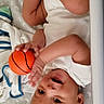 baby, infant, basketball, crib, smiling, happy, child, playing, toy, blanket, pattern, bed, clothing, hand, foot, person, cute, indoor, sleeping_area, expression