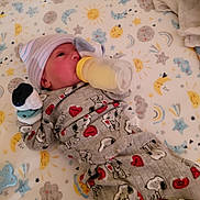 John is registered to the contest to win money with this photo: baby, newborn, crib, bottle, feeding, pajamas, hat, sleepwear, infant, cute, snoopy, stars, moon, sun, clouds, blanket, sleep, child, indoors, resting