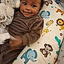 baby, child, stuffed_animal, plush_toy, brown_clothing, smile, face, hand_motion, animal_pillow, elephant, lion, giraffe, monkey, tiger, crocodile, heart_shapes, curly_hair, couch, indoor, cute